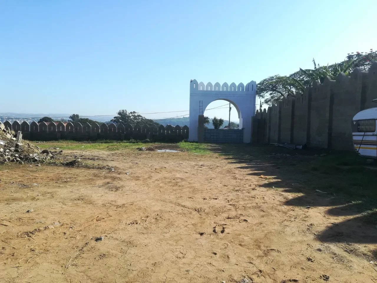 Project site — arched gateway with crenellated perimeter wall and Durban valley backdrop