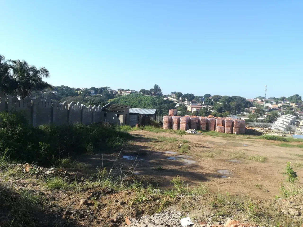 Project site — construction site with crenellated perimeter wall, stacked bricks and Durban hillside
