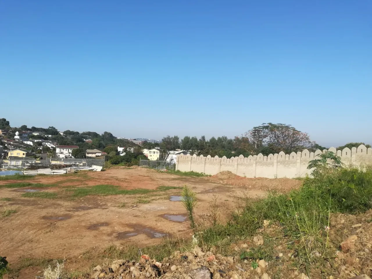 Project site — cleared site with crenellated boundary wall and Durban suburban backdrop