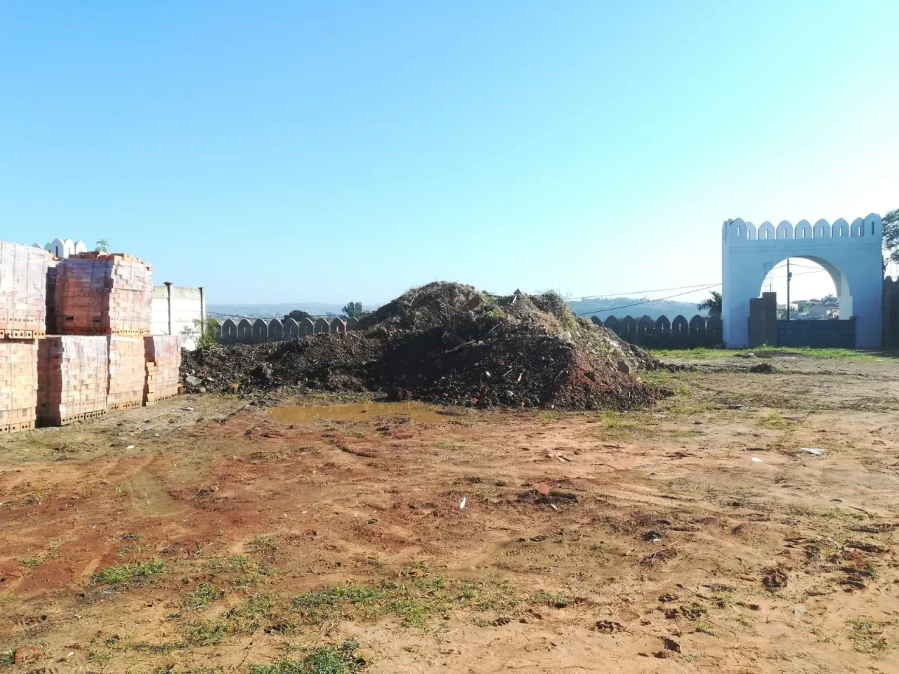 Project site — cleared site with arched gateway, stacked bricks and crenellated perimeter wall