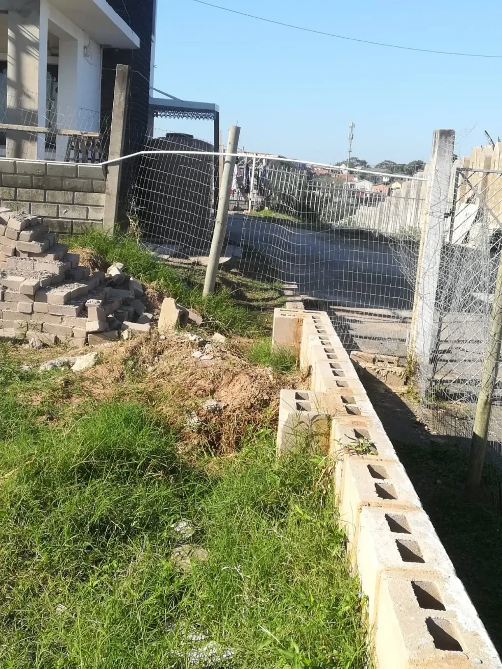 Project site — low concrete block boundary wall under construction along road