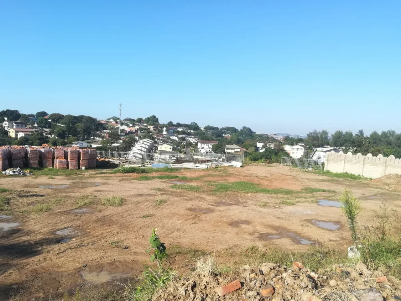 Project site — wide cleared site with stacked bricks, crenellated wall and Durban valley