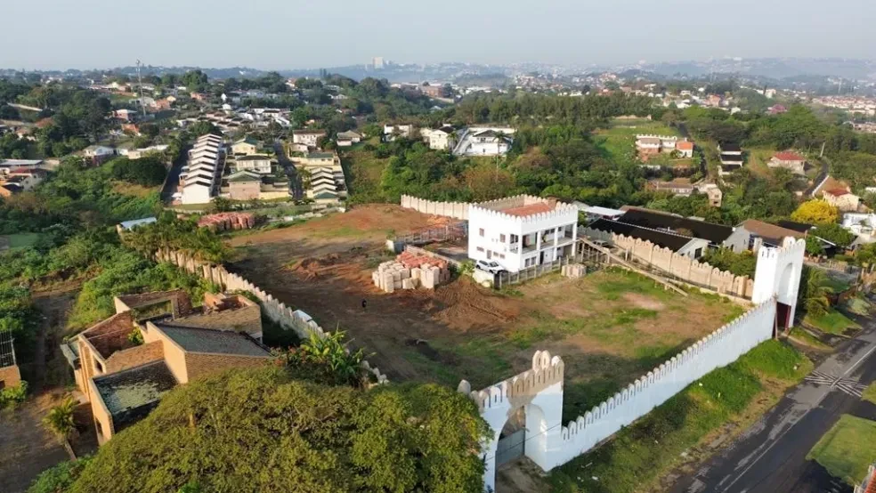 Project site — aerial view of white crenellated compound with cleared site and Durban suburb