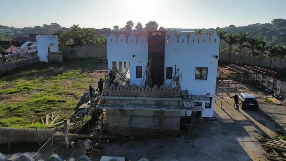Project site — aerial view of white crenellated building with workers on scaffolding and palm trees