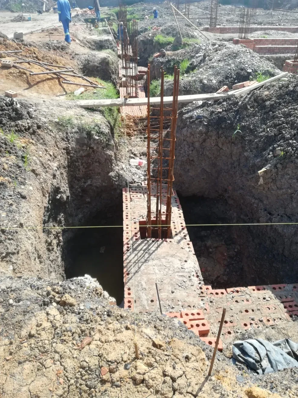 Project site — foundation excavation with rebar columns and crenellated building in background