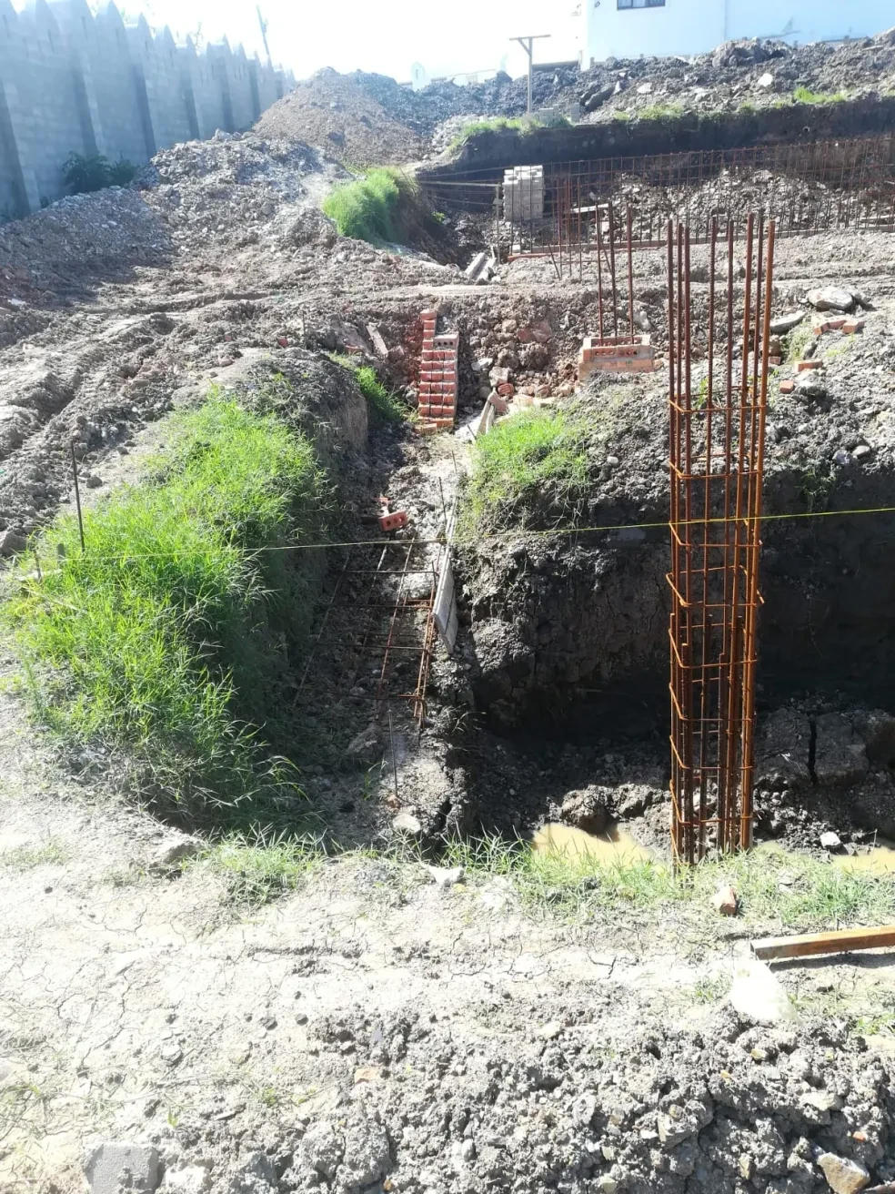 Project site — workers in excavation pit laying bricks around rebar column