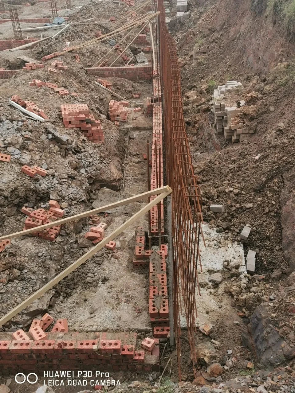 Project site — large foundation excavation with rebar grid and crenellated perimeter wall, Durban suburb in background