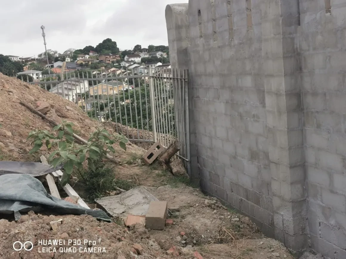 Project site — construction site with concrete block boundary wall and Durban hillside suburb