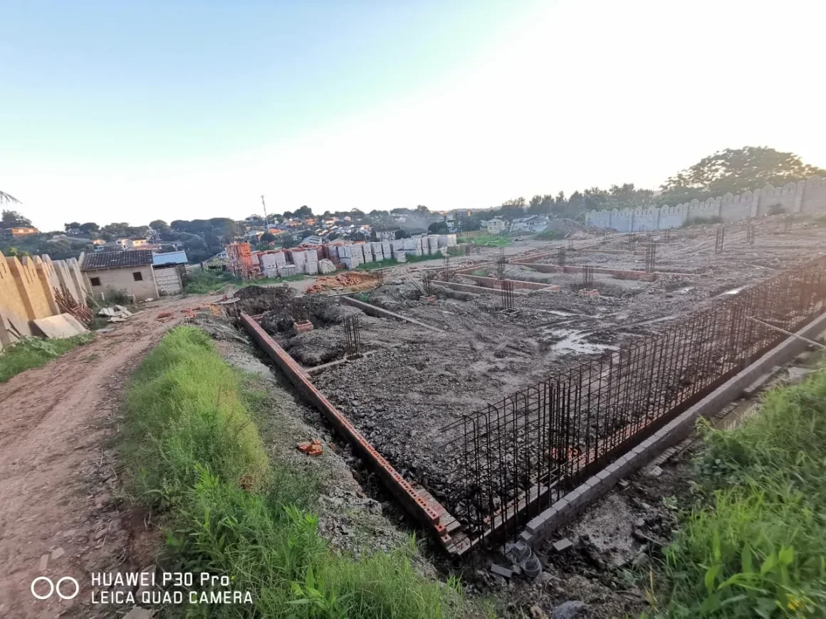 Project site — wide foundation excavation with rebar columns and crenellated perimeter wall at dusk