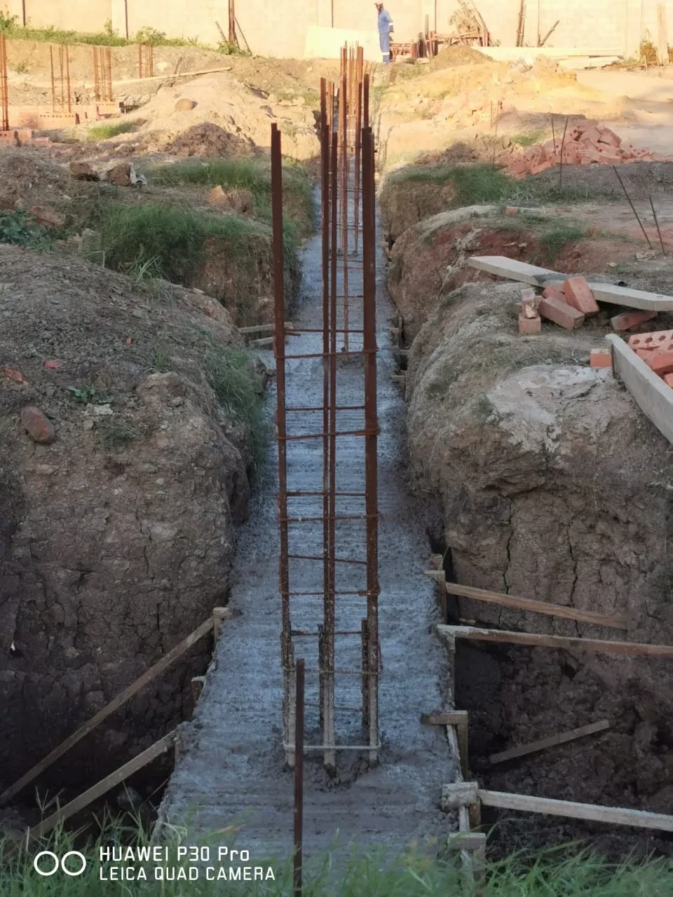 Project site — foundation trench with rebar reinforcement and crenellated wall with palm trees at dusk