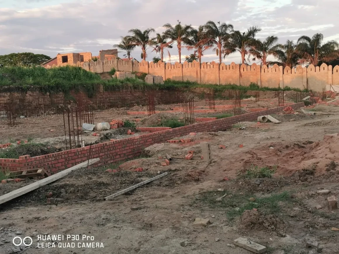 Project site — brick foundation walls with rebar columns and crenellated perimeter wall with palm trees at sunset
