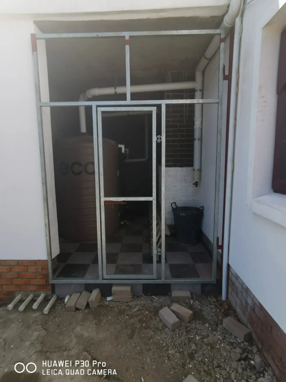 Project site — interior utility room with framed glass door installation, water tank and pipework