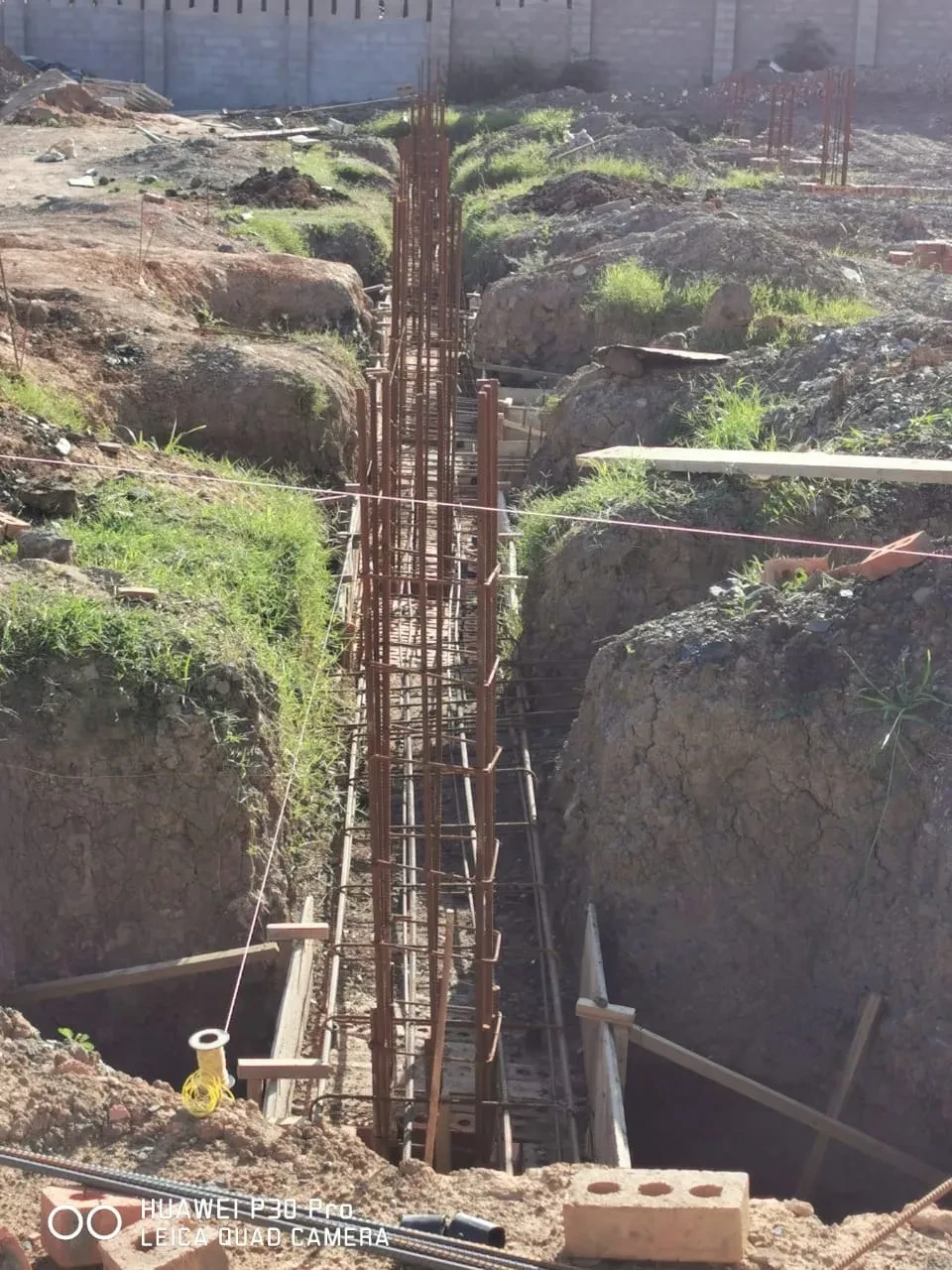 Project site — deep foundation trench with tall rebar cage and concrete block wall in background