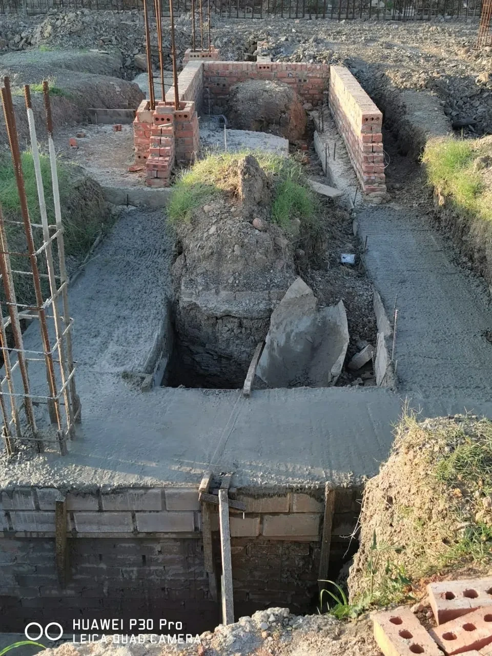 Project site — foundation pit with brick columns, rebar, and freshly poured concrete slab