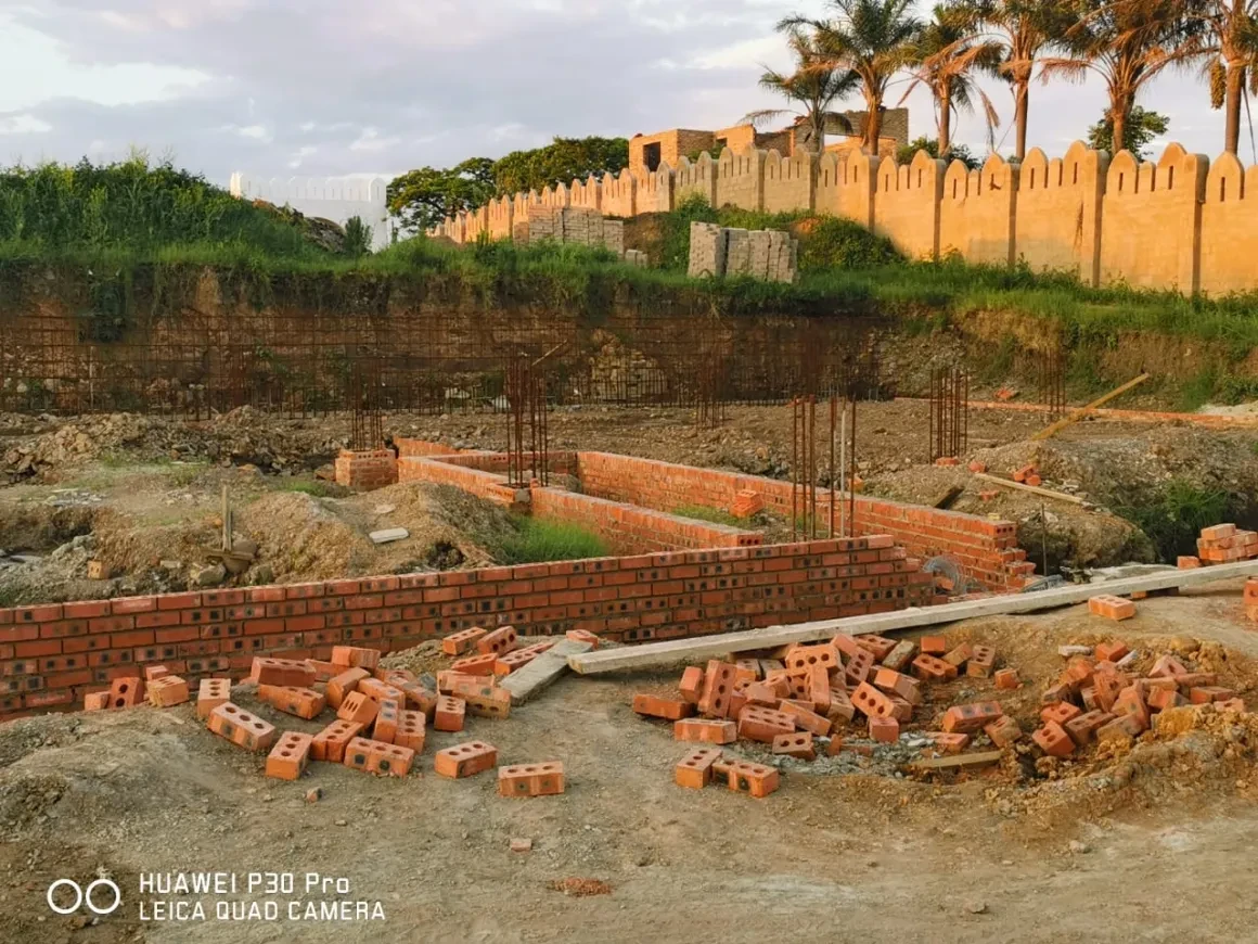 Project site — brick foundation walls with rebar columns and crenellated perimeter wall at golden hour