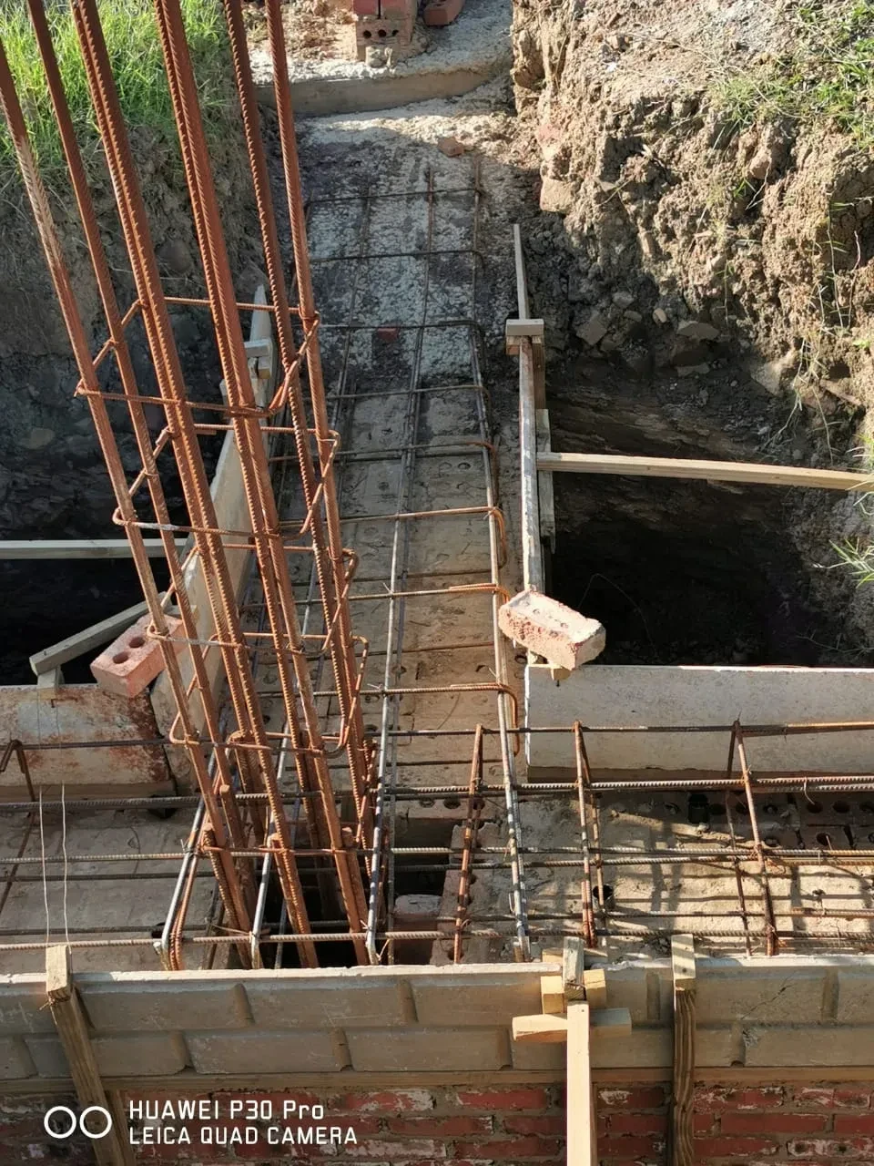Project site — rebar cage and concrete foundation trench with brick columns and wooden formwork