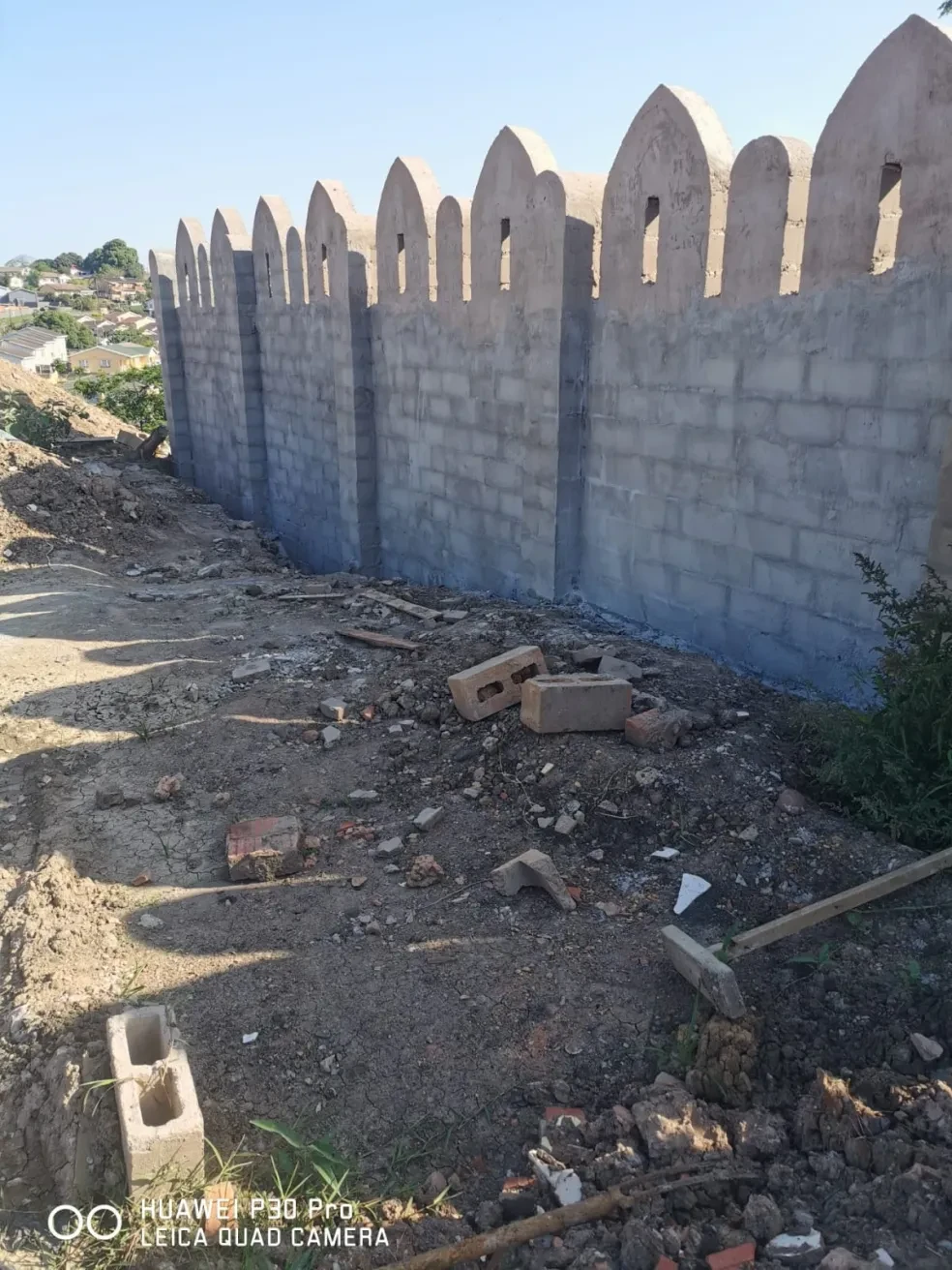 Project site — completed crenellated perimeter wall with arched parapets and Durban suburb behind