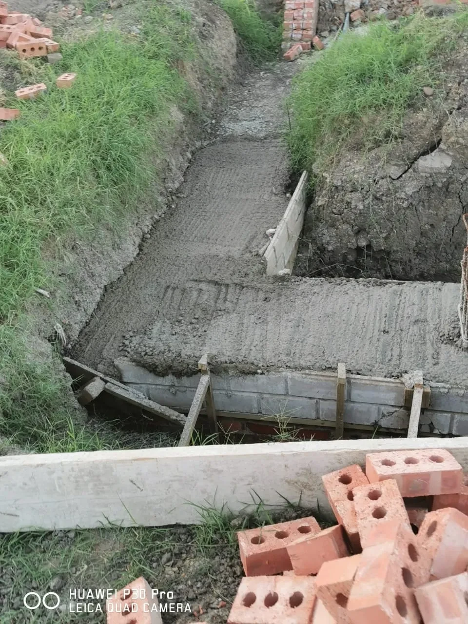 Project site — concrete foundation trench with drainage channel and overgrown vegetation