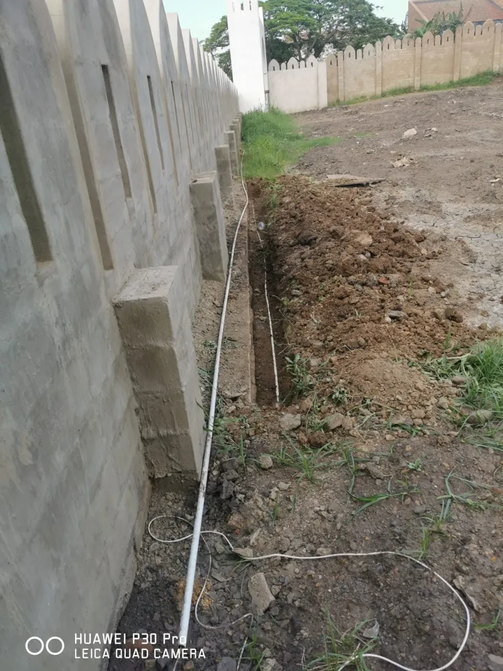 Project site — concrete wall foundation with electrical conduit trench alongside crenellated perimeter