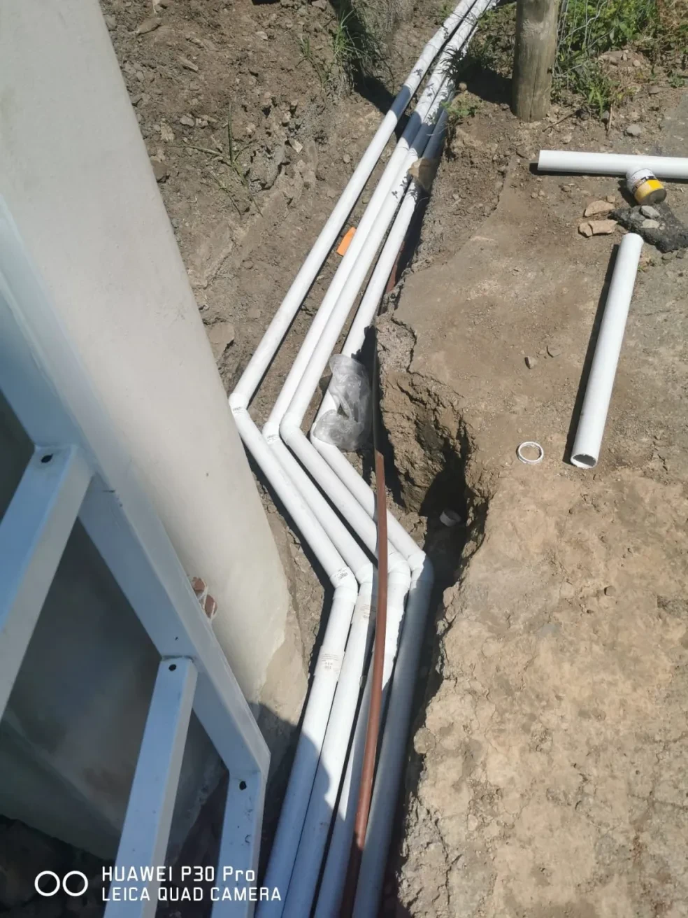 Project site — underground utility conduit pipes laid in trench alongside steel security gate