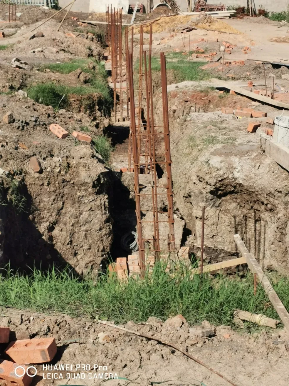 Project site — multiple PVC conduit pipes routed around corner in trench beside white building wall