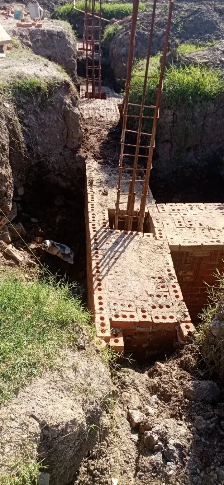 Project site — brick foundation walls with rebar columns across large cleared site, crenellated perimeter wall and palm trees