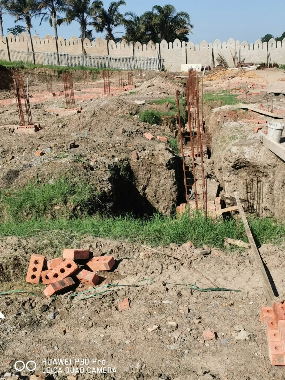 Project site — foundation excavation with brick column footings, rebar columns and white crenellated tower, person reviewing plans