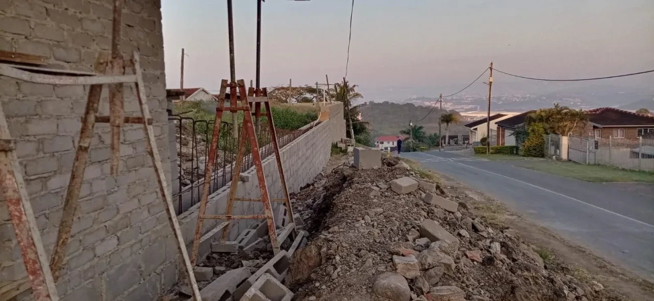 Project site — foundation excavation with rebar columns, brick footings and crenellated perimeter wall with palm trees