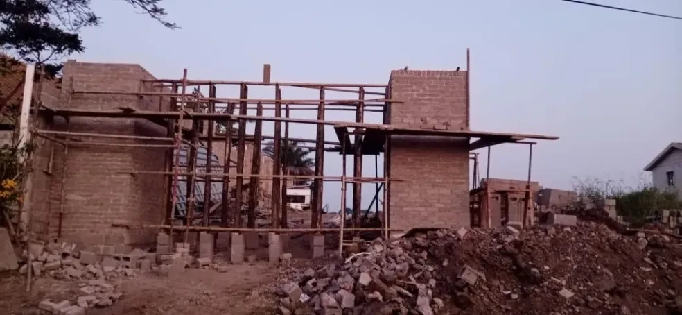 Project site — brick building with wooden scaffolding poles and crenellated parapet at dusk