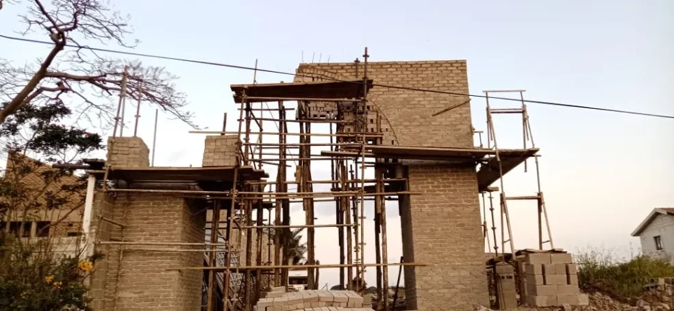 Project site — brick arch gateway under construction with dense bamboo scaffolding at dusk
