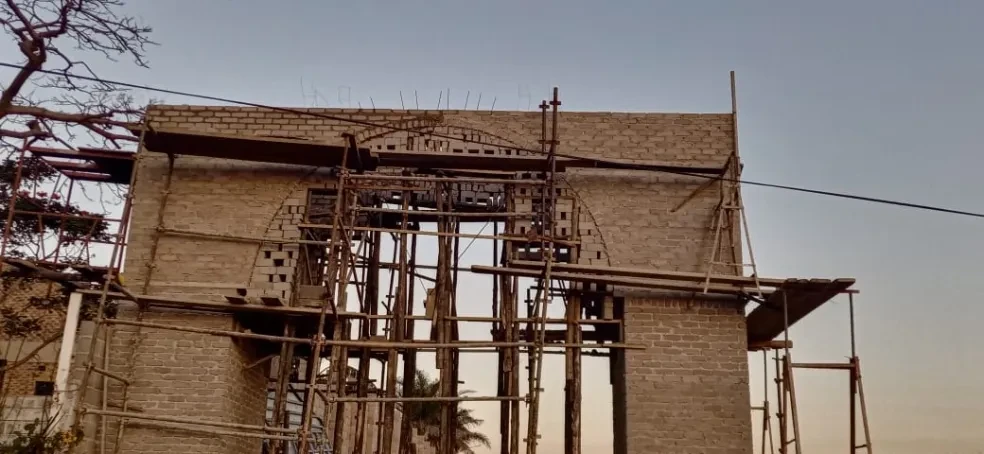 Project site — brick arch gateway with scaffolding, arch nearly complete with rebar spikes along parapet