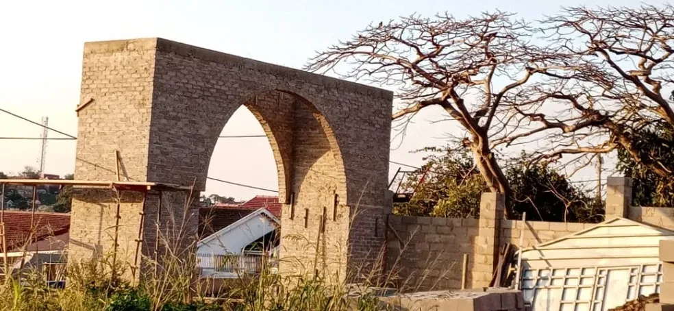 Project site — completed brick arch gateway with double pointed arches and crenellated parapet, bare tree alongside