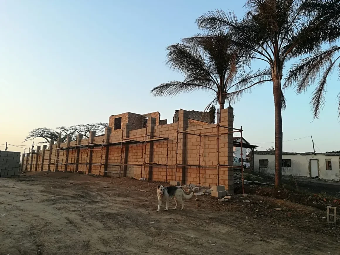 Project site — brick building under scaffolding with palm trees