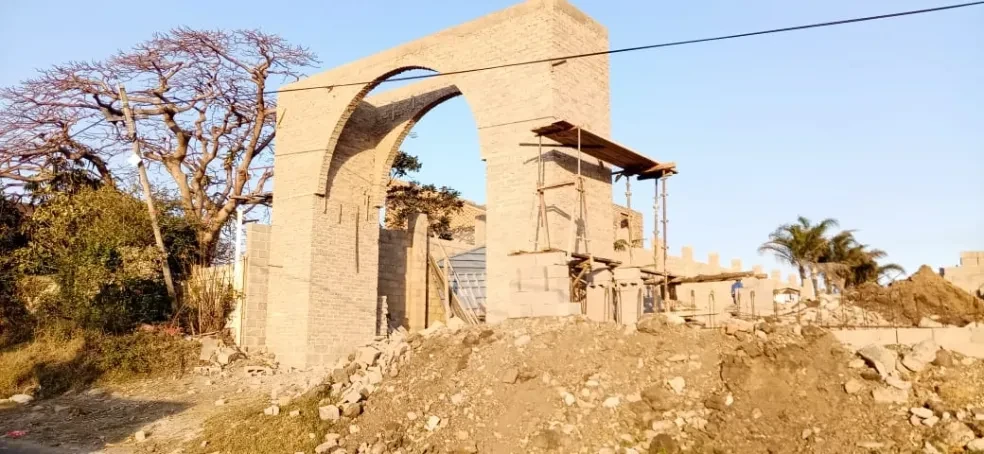 Project site — completed brick arch gateway with single large arch, bare tree and suburban houses in background