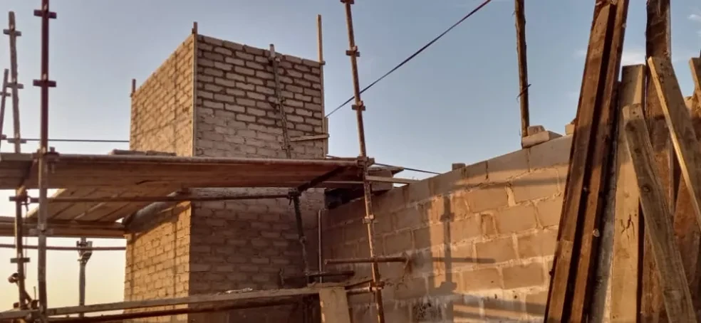 Project site — brick building under construction with scaffolding and wooden beams, clear sky