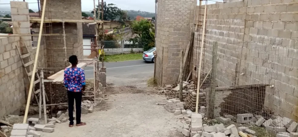 Project site — construction site with concrete block walls and person in blue floral shirt surveying progress