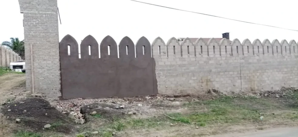 Project site — completed crenellated perimeter wall with dark gate panel and plastered pillar