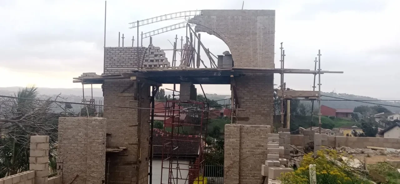 Project site — large brick arch gateway under construction with scaffolding and Durban suburb in background