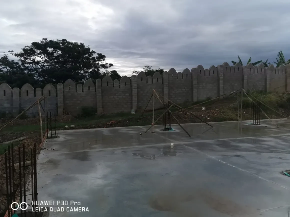 Project site — freshly poured concrete slab with rebar columns and crenellated perimeter wall with palm trees