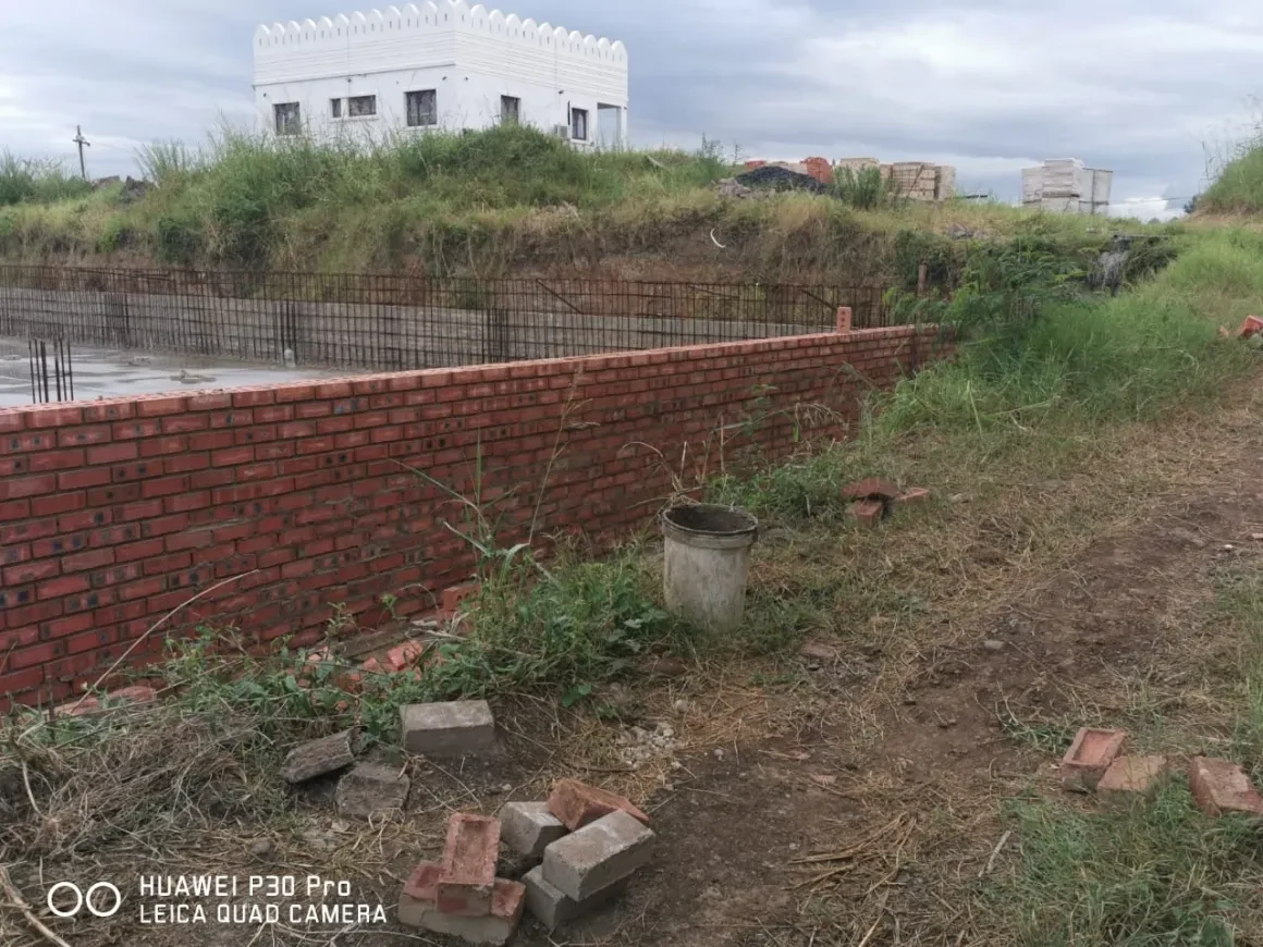 Project site — brick retaining wall with rebar columns alongside concrete slab, white crenellated building behind