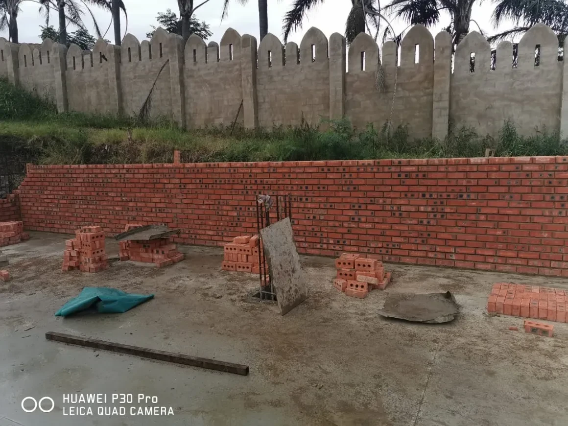 Project site — brick foundation wall on concrete slab with stacked building materials and Durban suburb in background