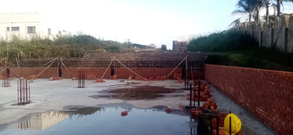 Project site — concrete slab with rebar columns, brick foundation walls and yellow hard hat in foreground