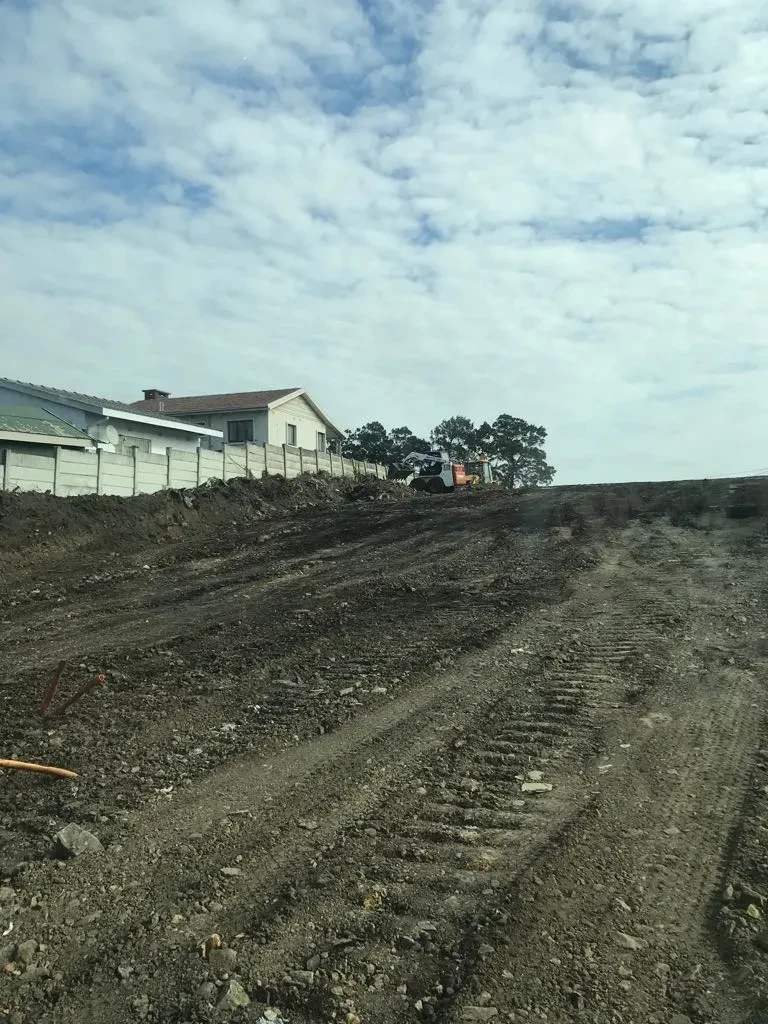 Project site — wide cleared site with concrete perimeter wall, residential houses and Durban suburb in background