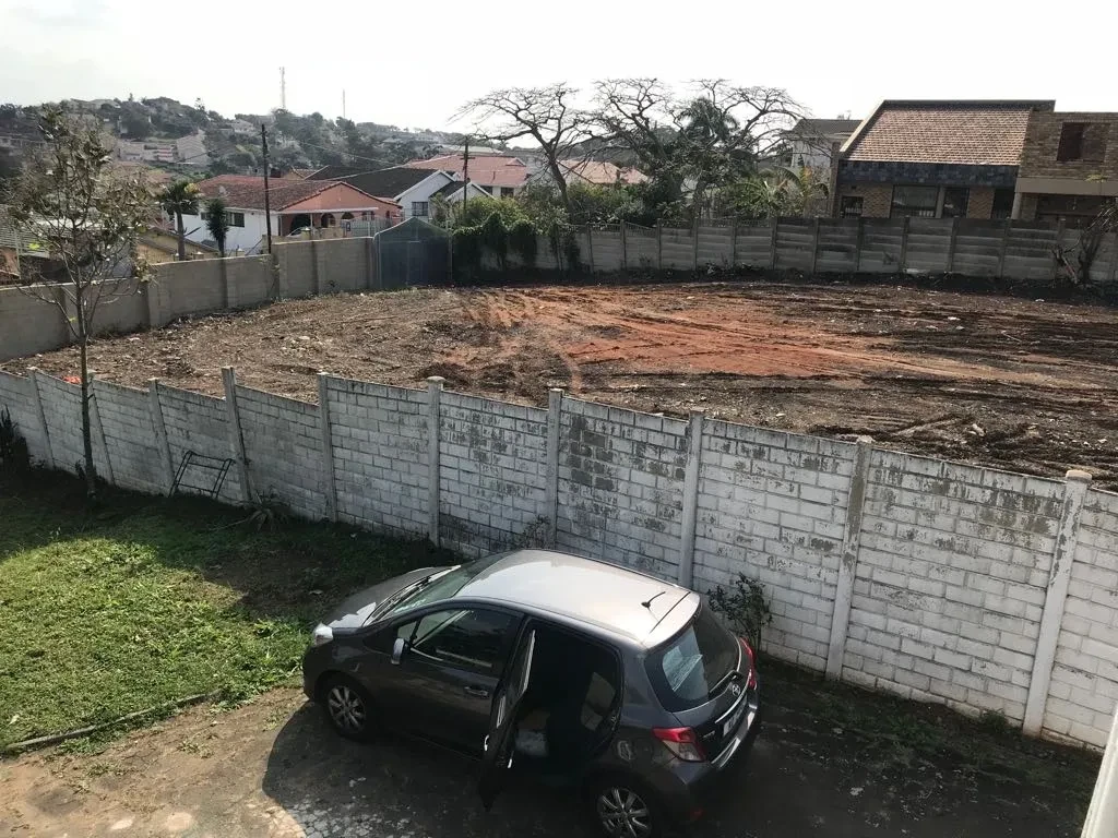 Project site — cleared site with concrete perimeter wall and car parked in foreground, Durban suburb behind