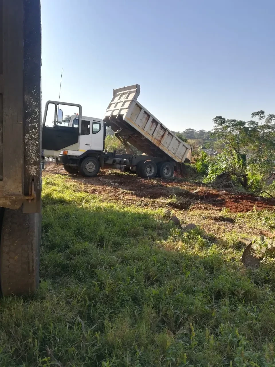Project site — white dump truck with raised bed tipping soil on hillside construction site