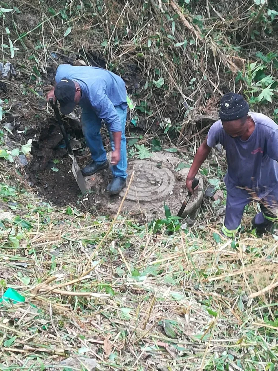Project site — worker clearing overgrown land with timber, pipes and construction debris in foreground