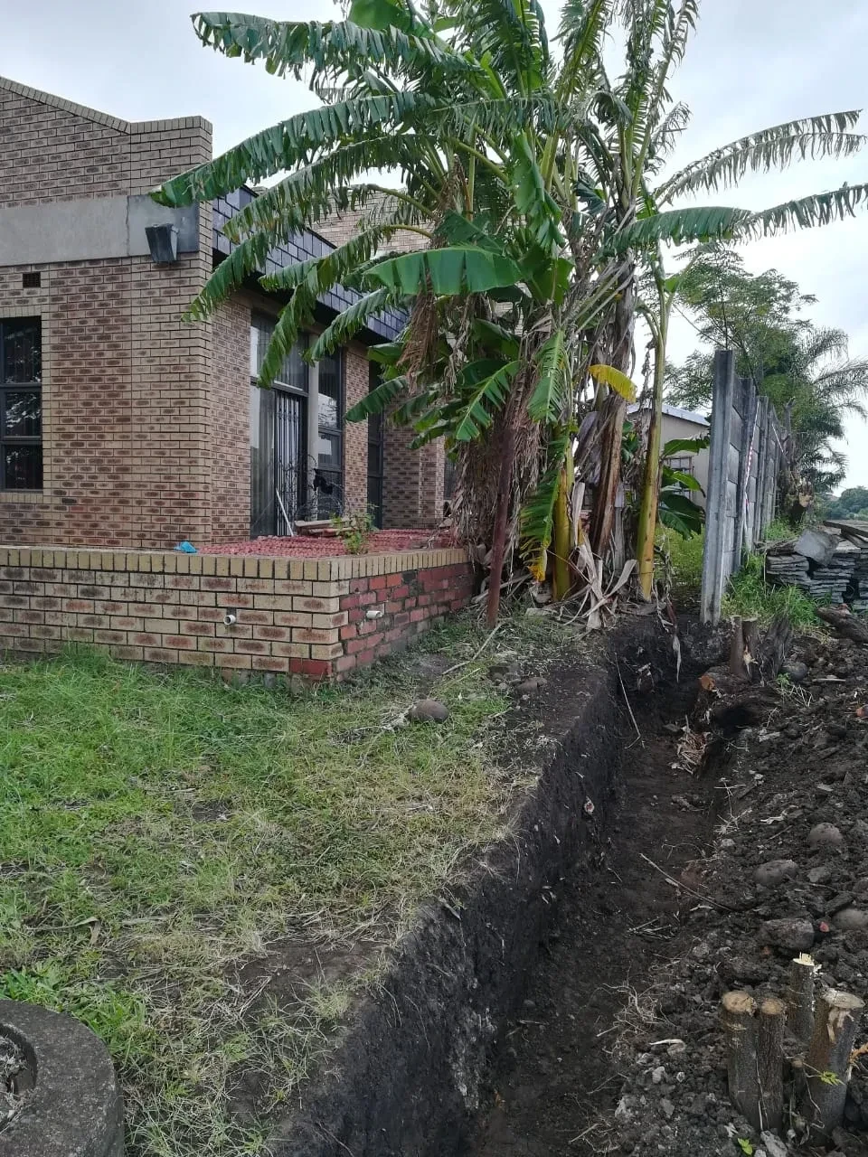 Project site — brick building under construction rising above concrete precast boundary wall, overcast sky