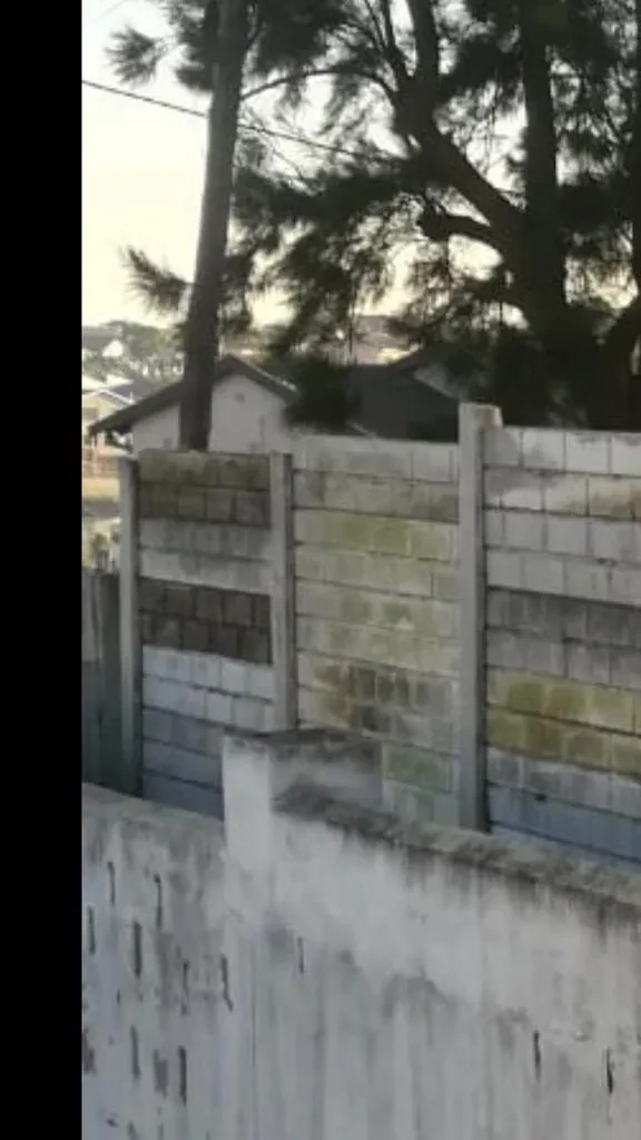 Project site — brick building under construction with open window aperture rising above concrete precast boundary wall
