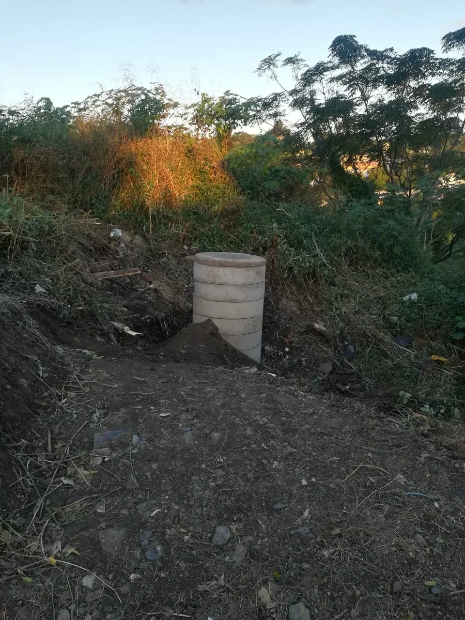 Project site — stacked concrete manhole rings installed in excavated trench on cleared hillside site at dusk