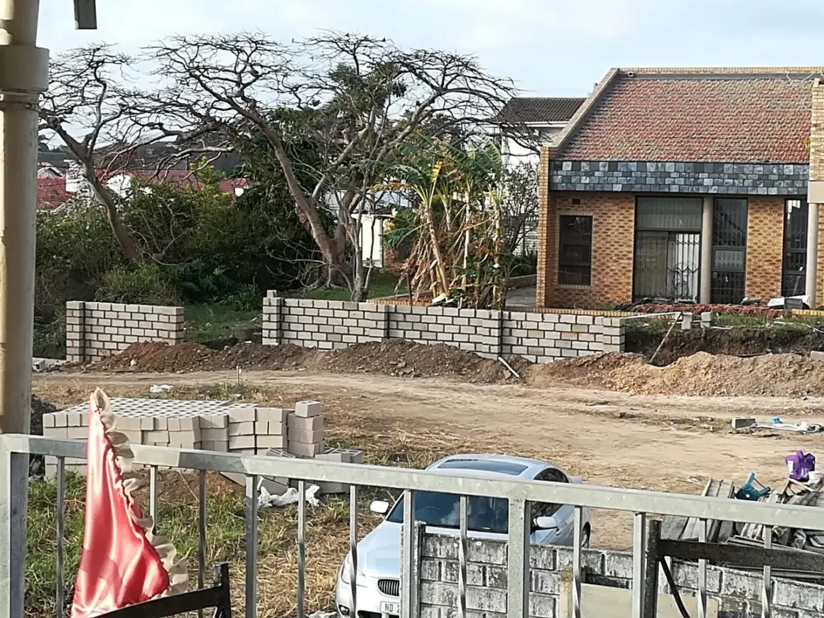 Project site — brick wall construction with residential backdrop